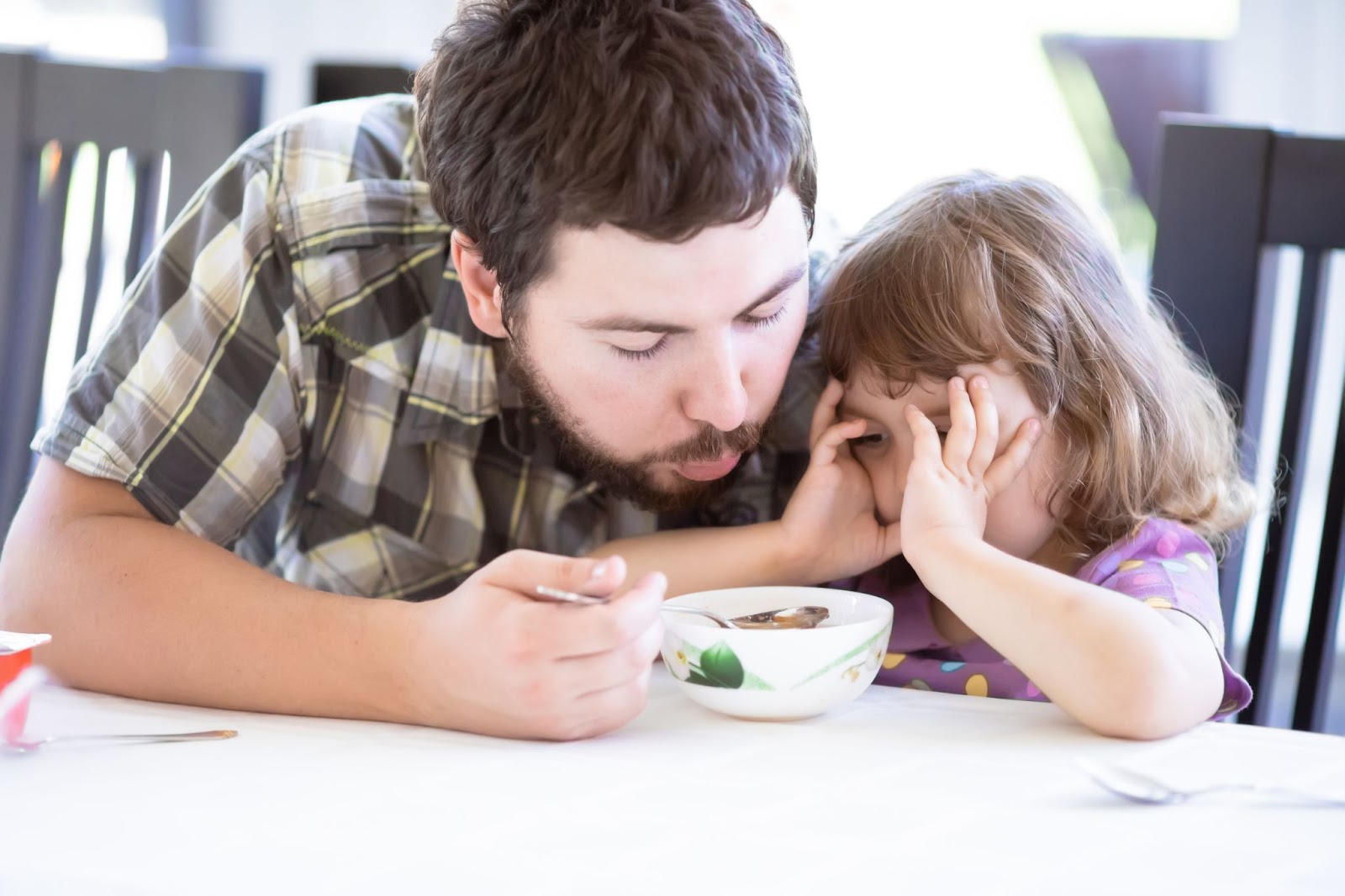 Un padre intentando convencer a su hija de comer sopa concepto trastornos alimentarios