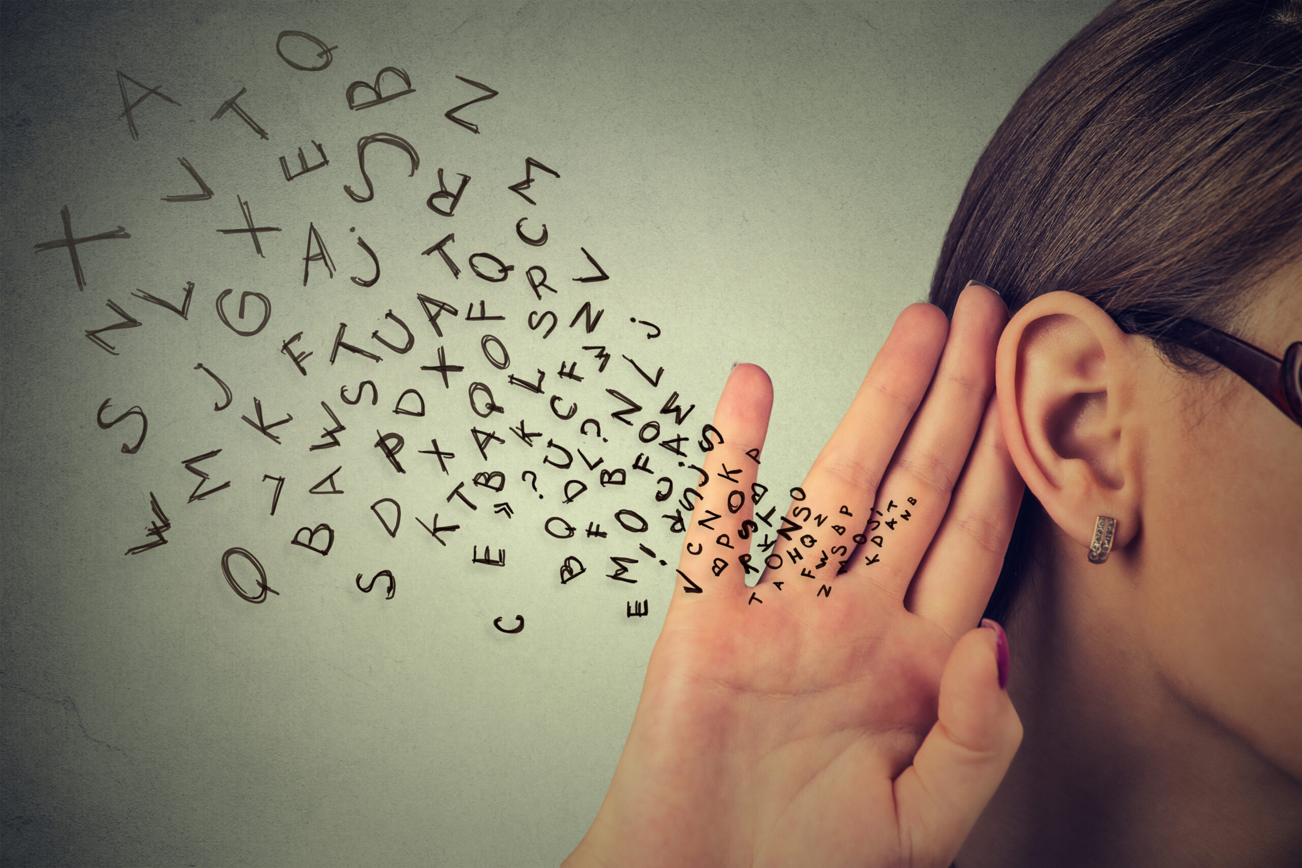 Une femme met sa main à l’oreille alors que des petites lettres de l’alphabet se dirigent vers sa main.