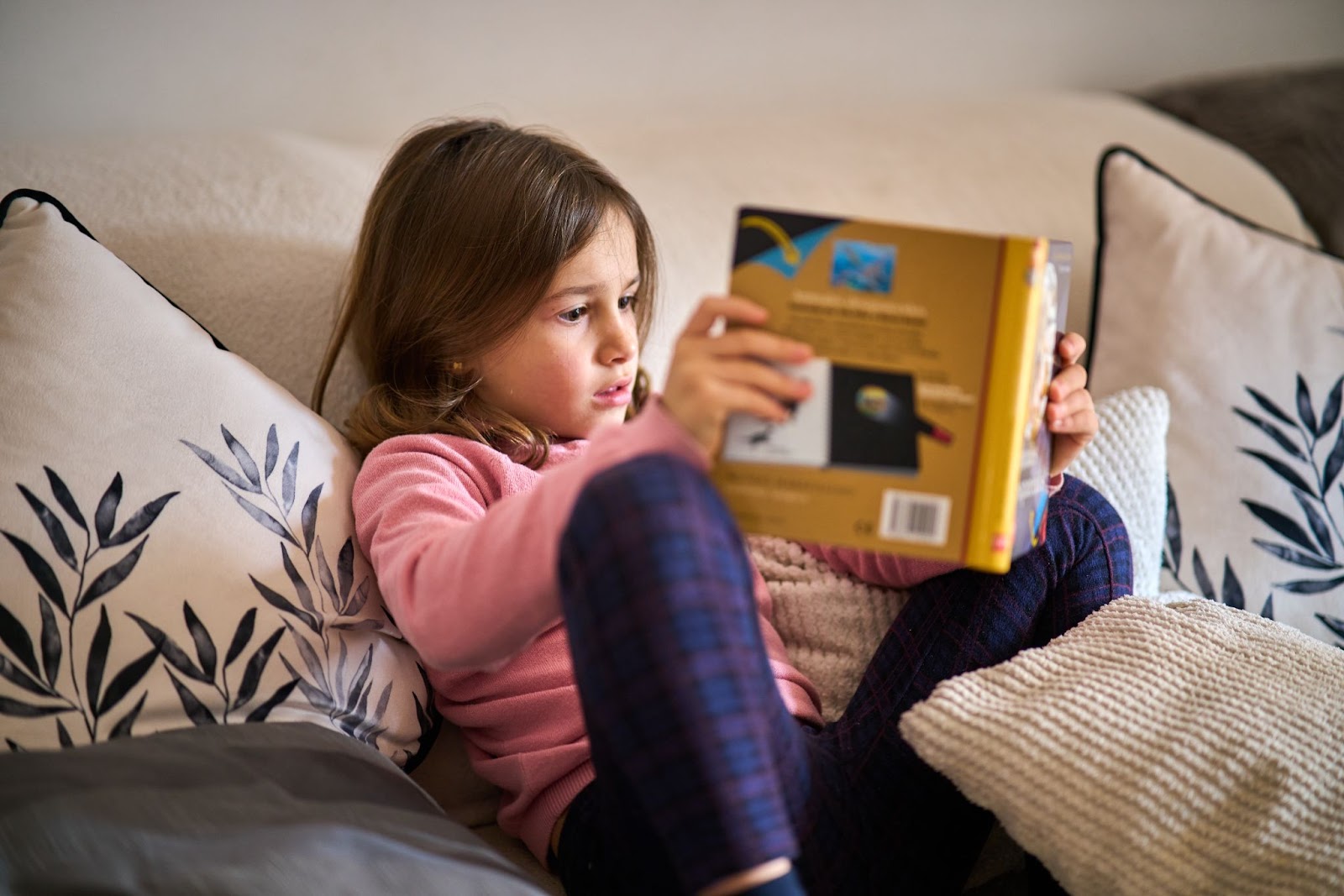Una bambina seduta su un divano a leggere un libro