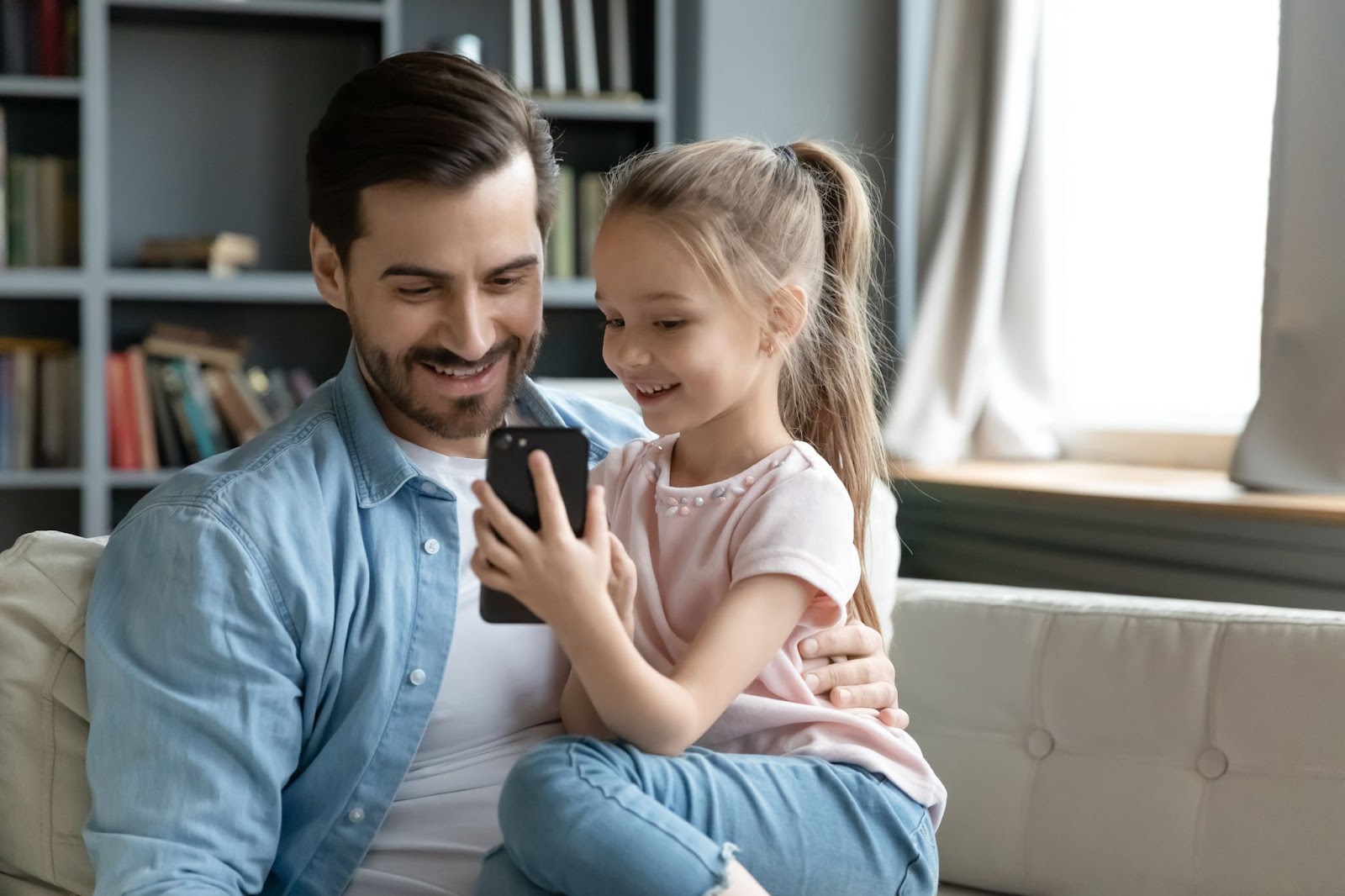 Una giovane ragazza mostra al padre qualcosa sul suo cellulare